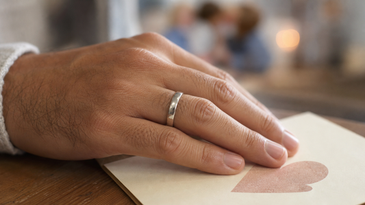 Man wearing a promise ring on his finger, with a blurred heartfelt message card in the background, symbolizing commitment and deep emotion.