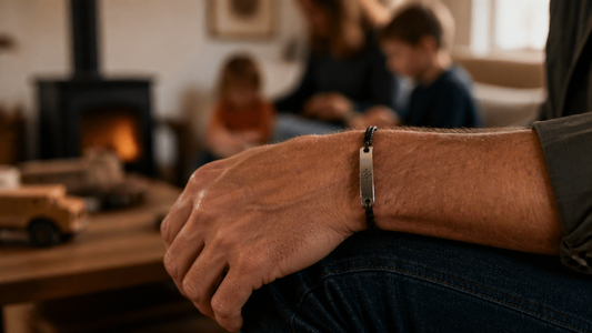 Man wearing a personalized leather and metal bracelet, subtly engraved with initials, in a warm, out-of-focus family home setting.