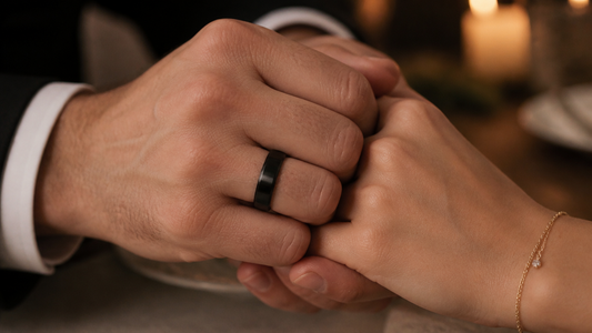 Man's hand wearing a black wedding band for him, holding a woman's hand