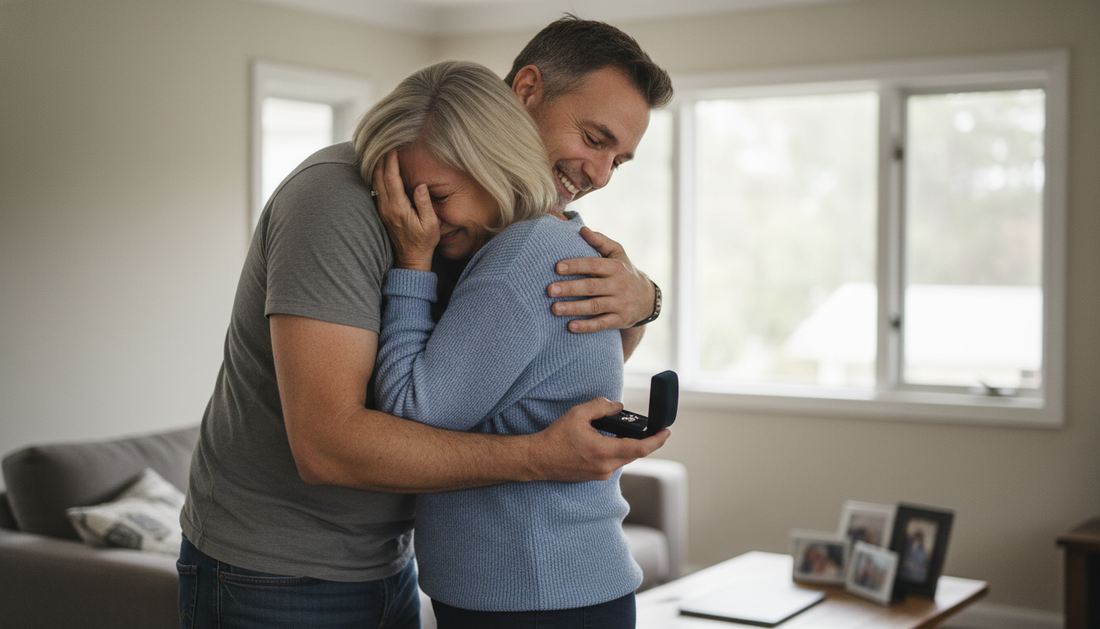 Adult son hugging his mom in the living room while she holds an open jewelry gift box, both emotional
